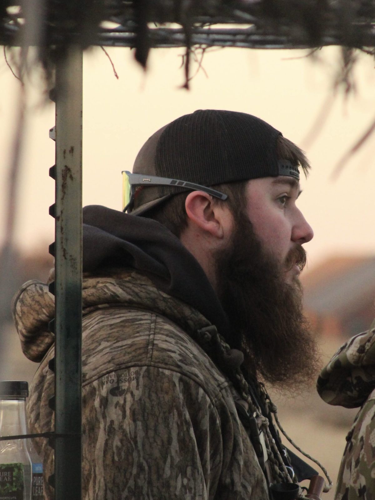 Guide Hunter Murphy in camo and a ball cap, looking out from the duck blind at first light