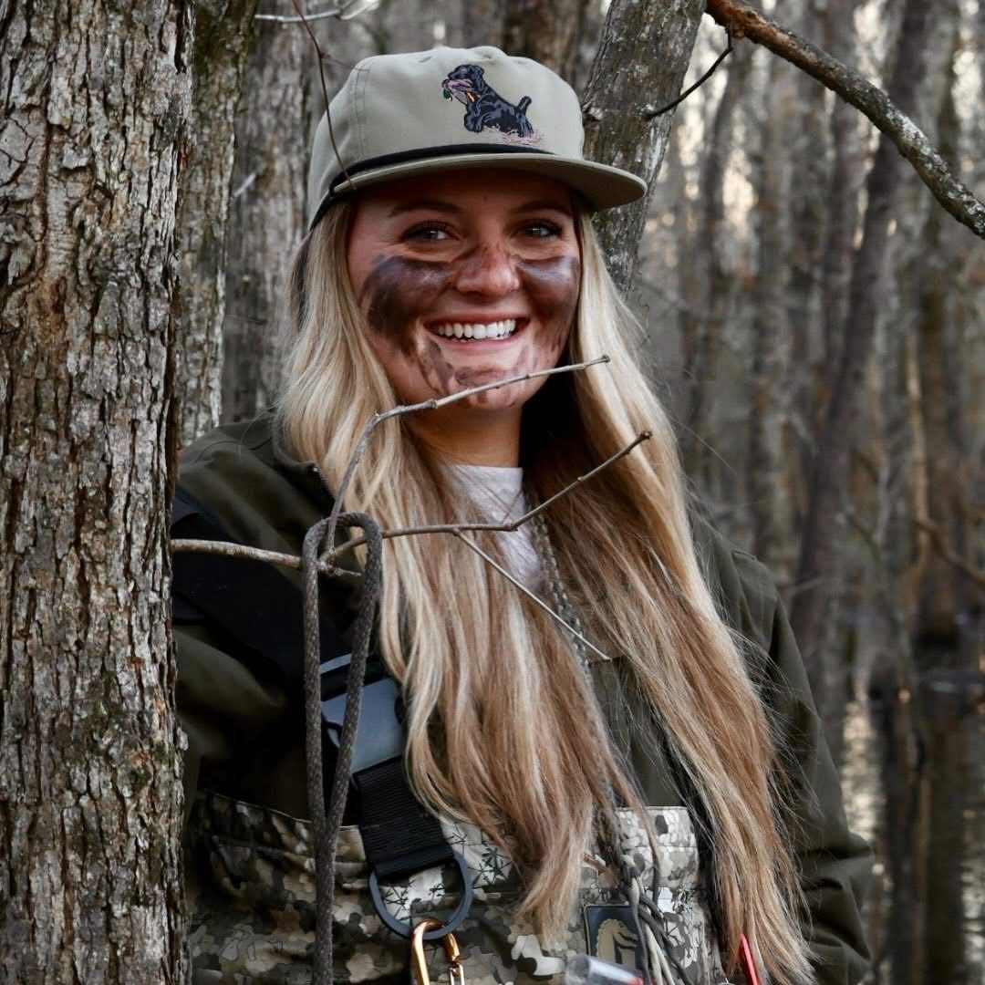 Avery Hughes in camo face paint and a ball cap, smiling from the timber